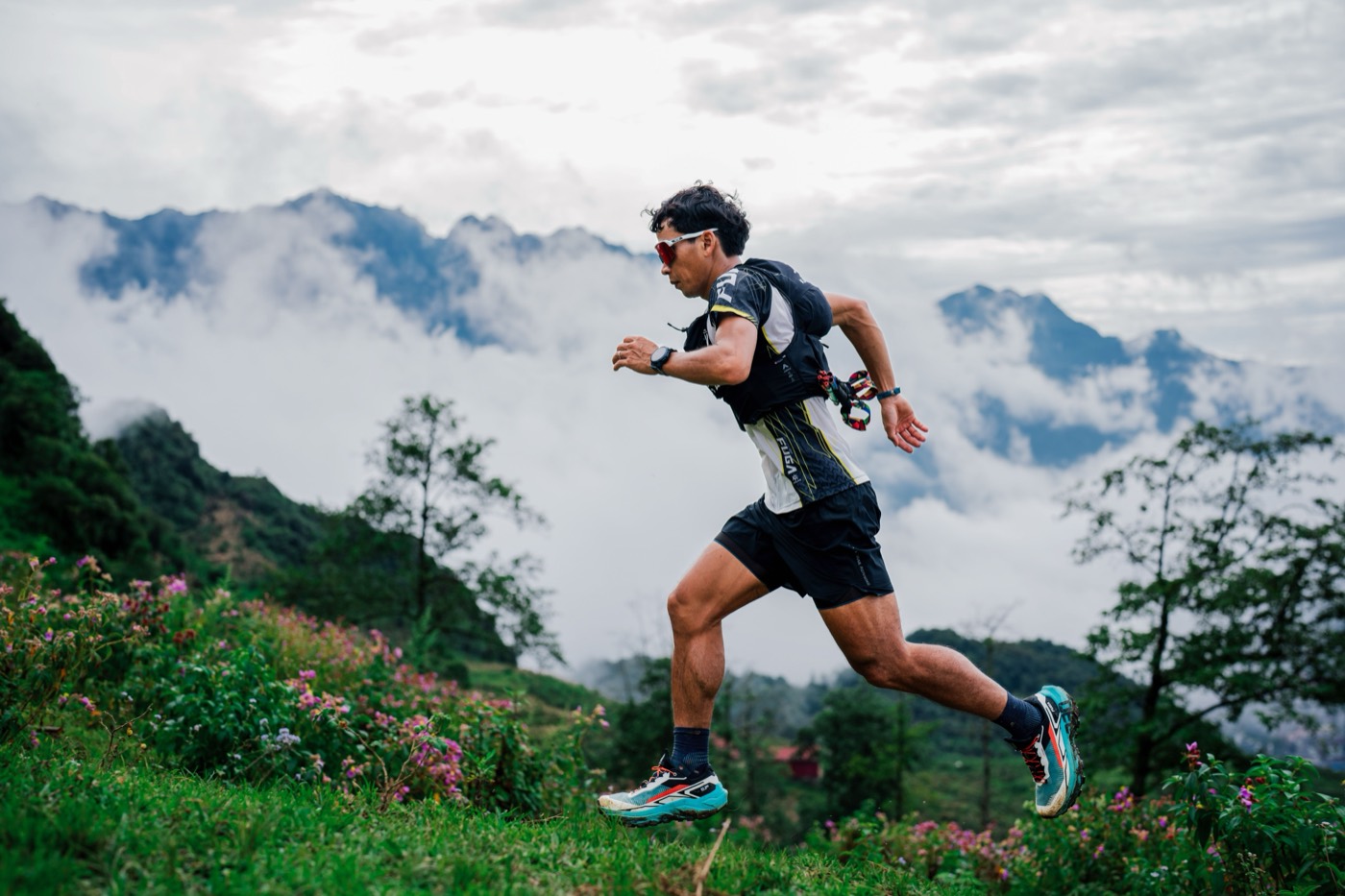 Coureur de trail sur une crête herbeuse, au-dessus d'une mer de nuages, sommets à l'arrière-plan.